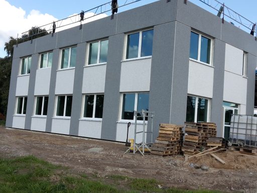 Neues Gebäudeeck mit großen Fenstern und Baustellenmaterial im Vordergrund.