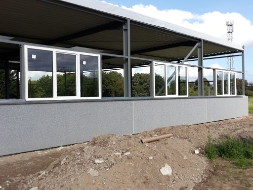 Eine Baustelle mit einem neuen Gebäude, das große Fenster und einen Erdboden zeigt.